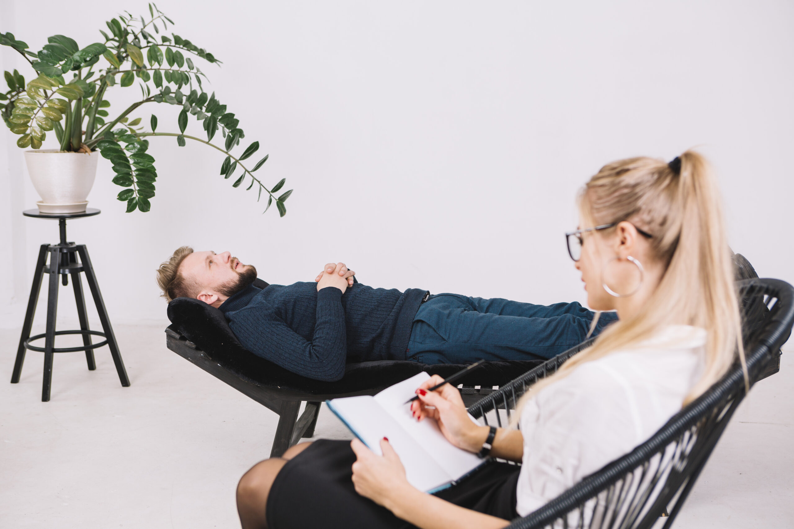 female-psychologist-writing-notes-diary-while-patient-lying-couch-clinic